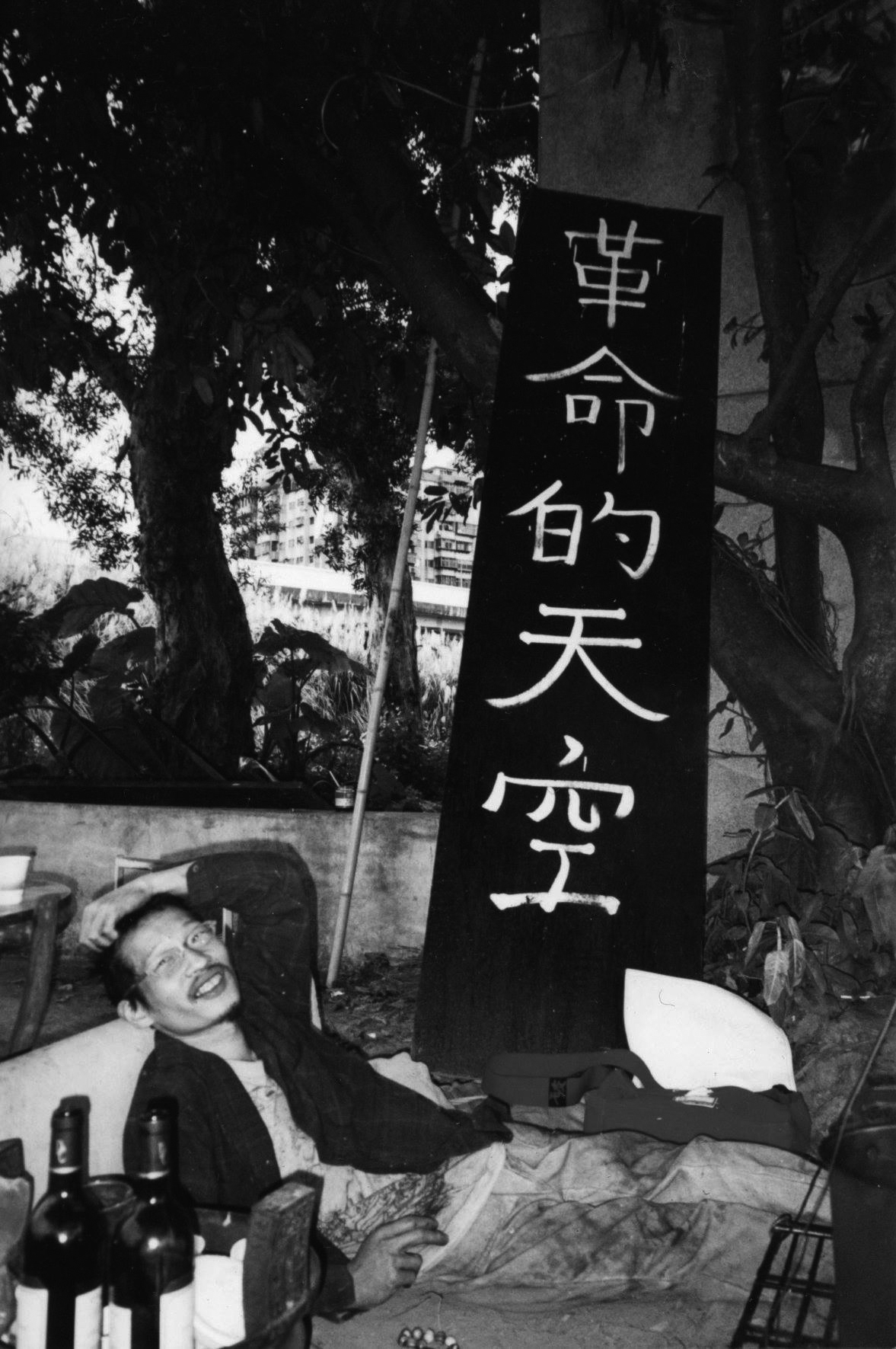 Wu Chung-Wei sitting next to a sign that reads “Revolutionary Skies” (革命的天空), at Huashan Arts District, Taipei, 2000. Photo Yao Jui-Chung.