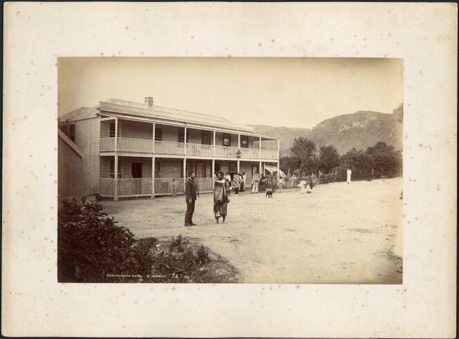 The Rotomahana Hotel, Te Wairoa, January 1885. Photograph by George Dobson Valentine. A Maori man wearing a korowai (tag cloak) and carrying a patu is standing in the foreground.