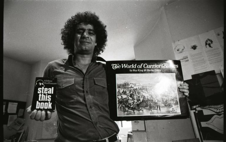 Abbie Hoffman holding copies of Steal This Book and The World of Currier and Ives